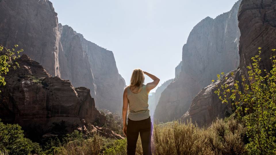 a woman looks into the sun between mountains