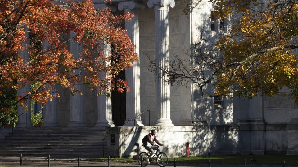 A man rides a bicyle past Whig Hall in autumn