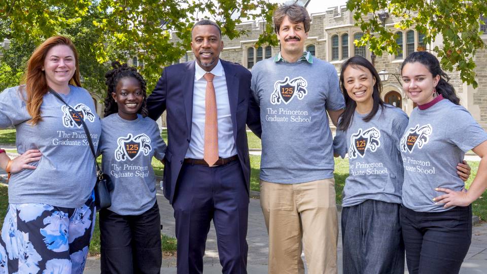Graduate School Dean Rodney Priestley poses with four students on campus on a sunny day.