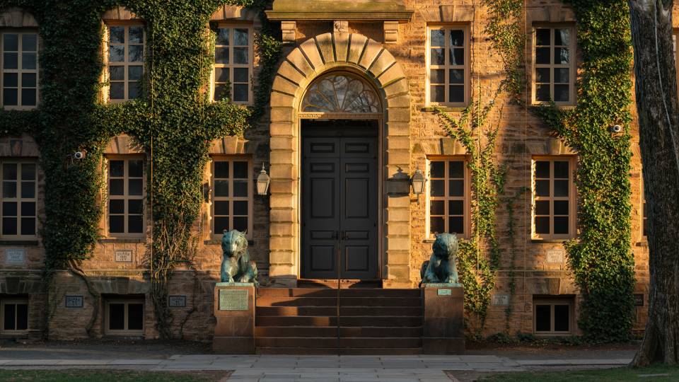 Nassau Hall at sunset with a warm glow over its bronze tiger sculptures