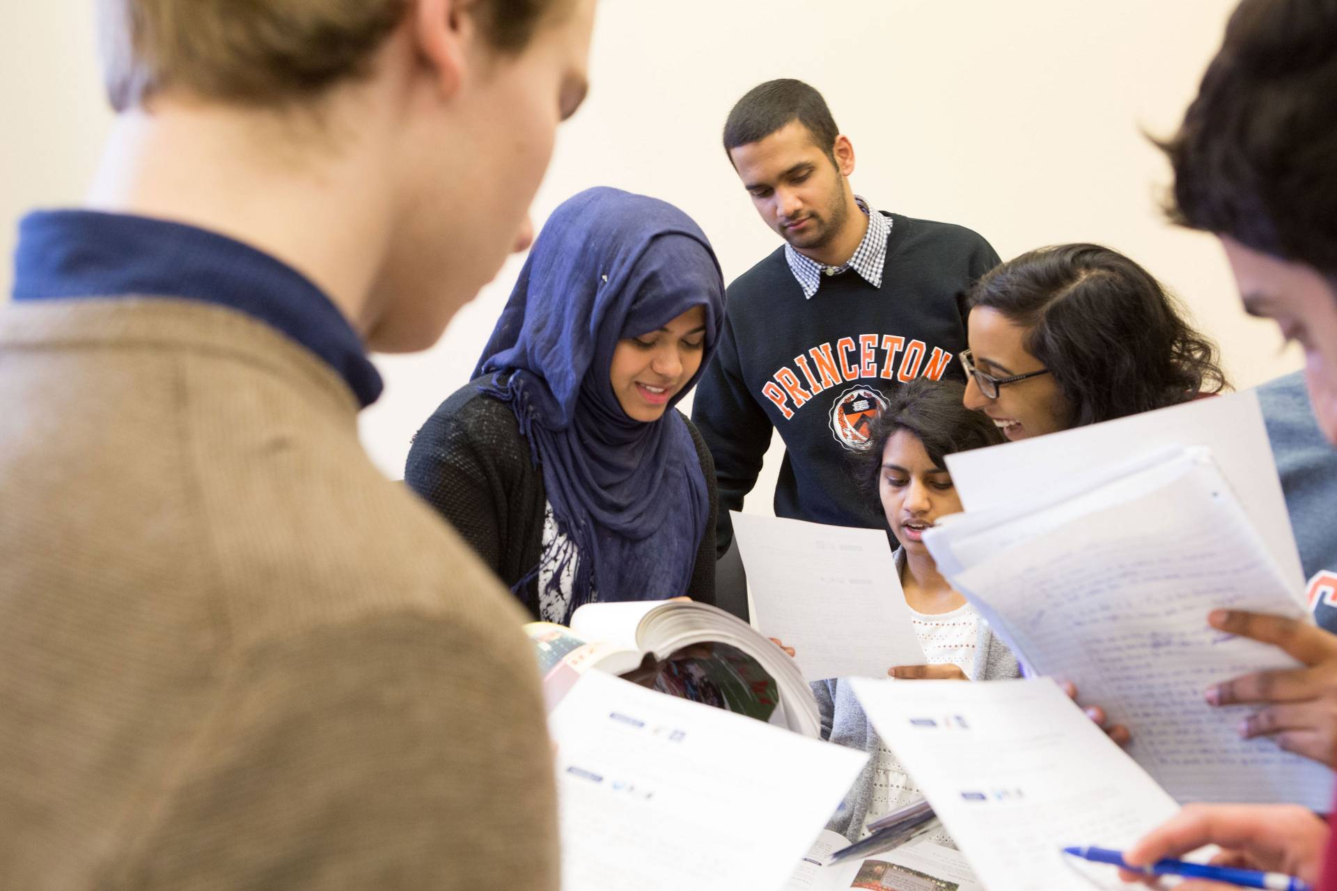 Students stand in a huddle discussing work on paper packets