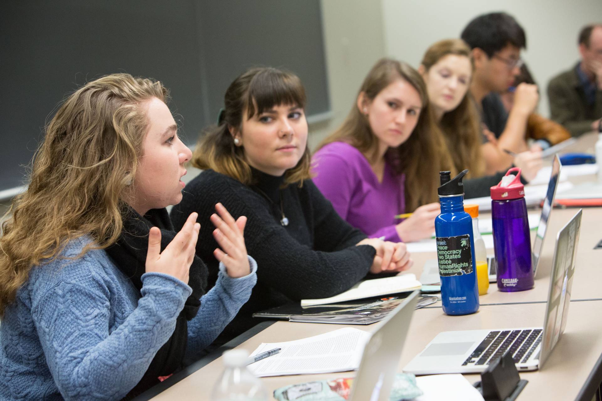 A student makes a point in a discussion with other students around a conference table in a classroom.