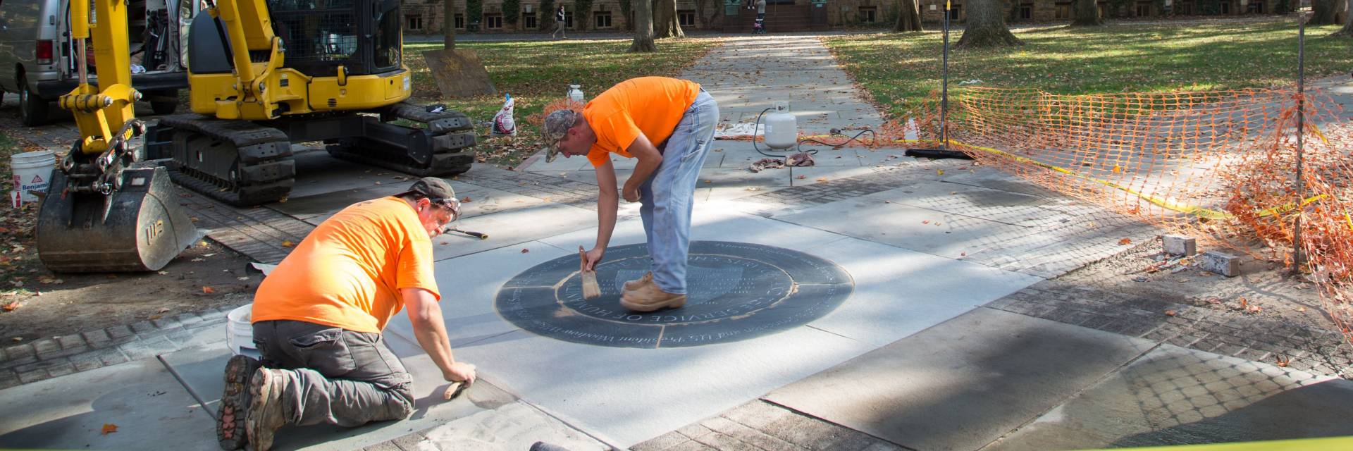 Workers installing University motto medallion outside Nassau Hall