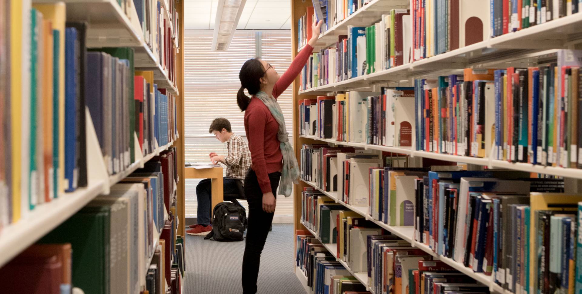 Student reaching for book on library shelf