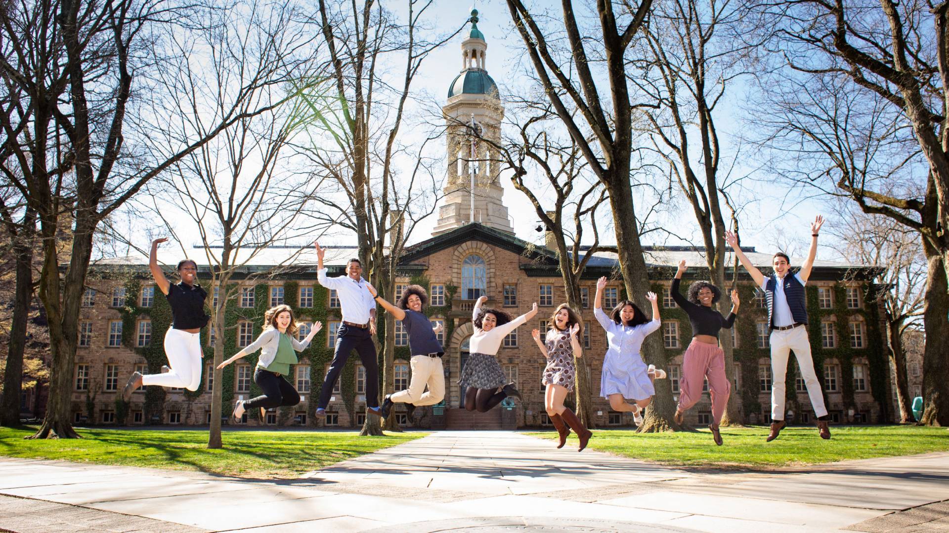 Maia Craver, Katie Tyler, Gaby Joseph, Jordan Thomas, Soraya Morales Nuñez, Allison Berger, Zoë Anne Toldedo, Christina Onianwa and Diego Negrón-Reichard leaping in the air in front of Nassau Hall