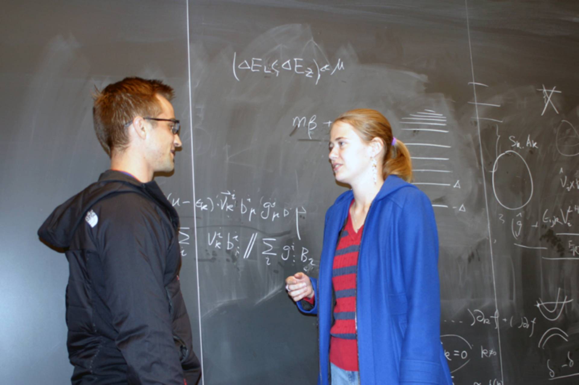 Ksenia Sokolova and Ryan Manzuk speak in front of a chalk board