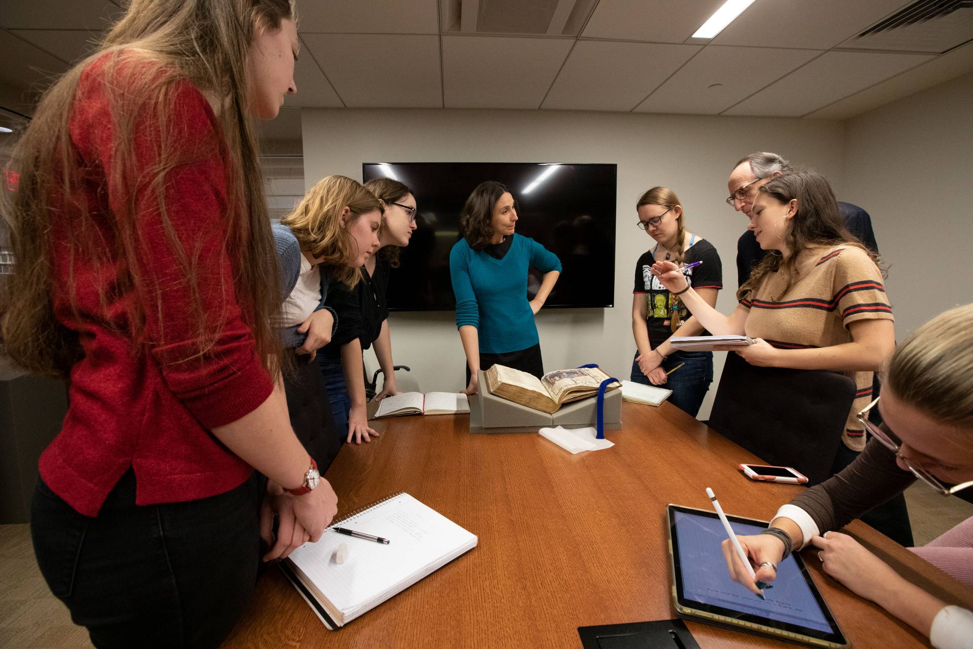 Students and professors looking at ancient illuminated manuscript