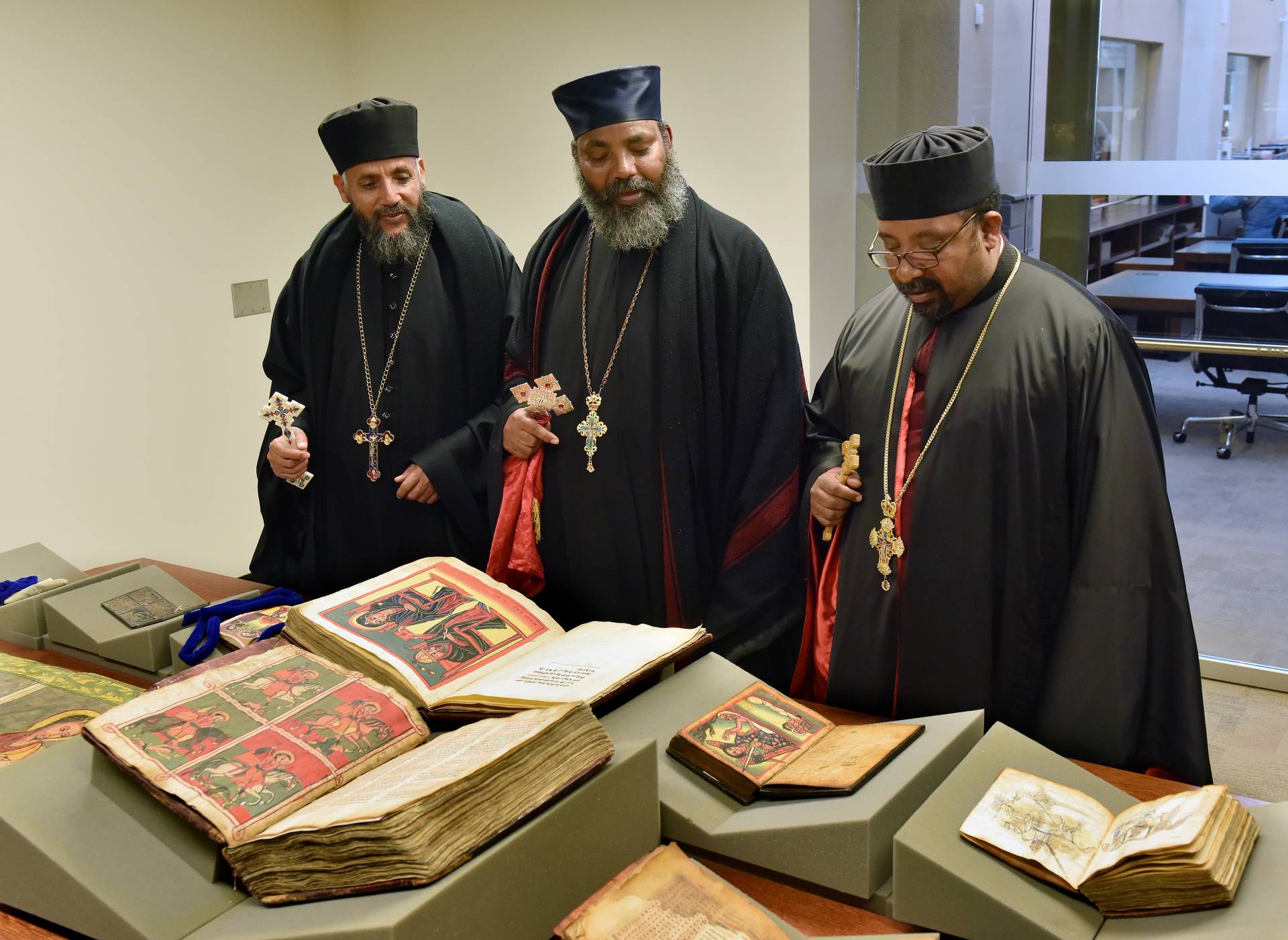 Three visiting priests looking at/discussing a manuscript on a table display
