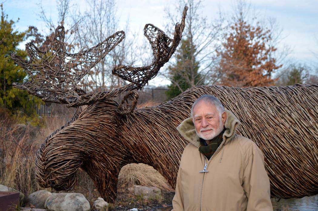 Robert Mark poses in front of a sculpture of a moose made of tree branches