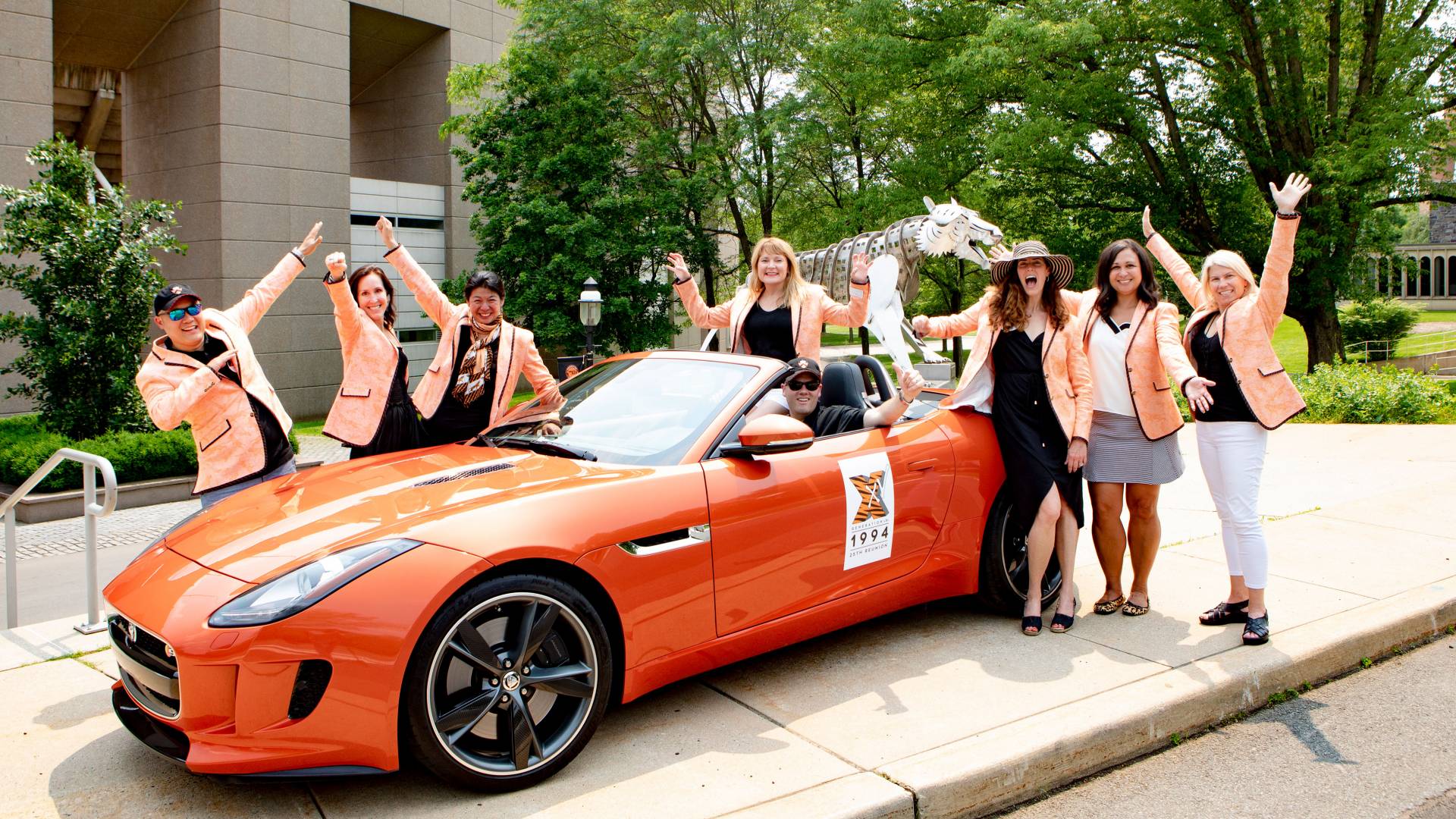 Alumni gather around an orange Jaguar car