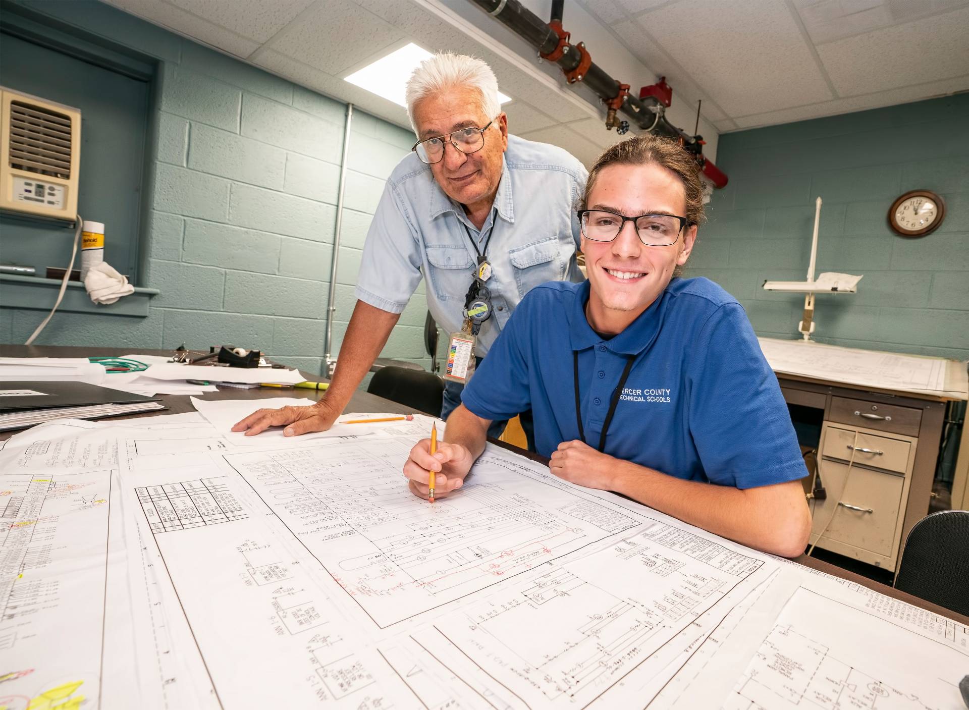A technician and apprentice look over blueprint plans