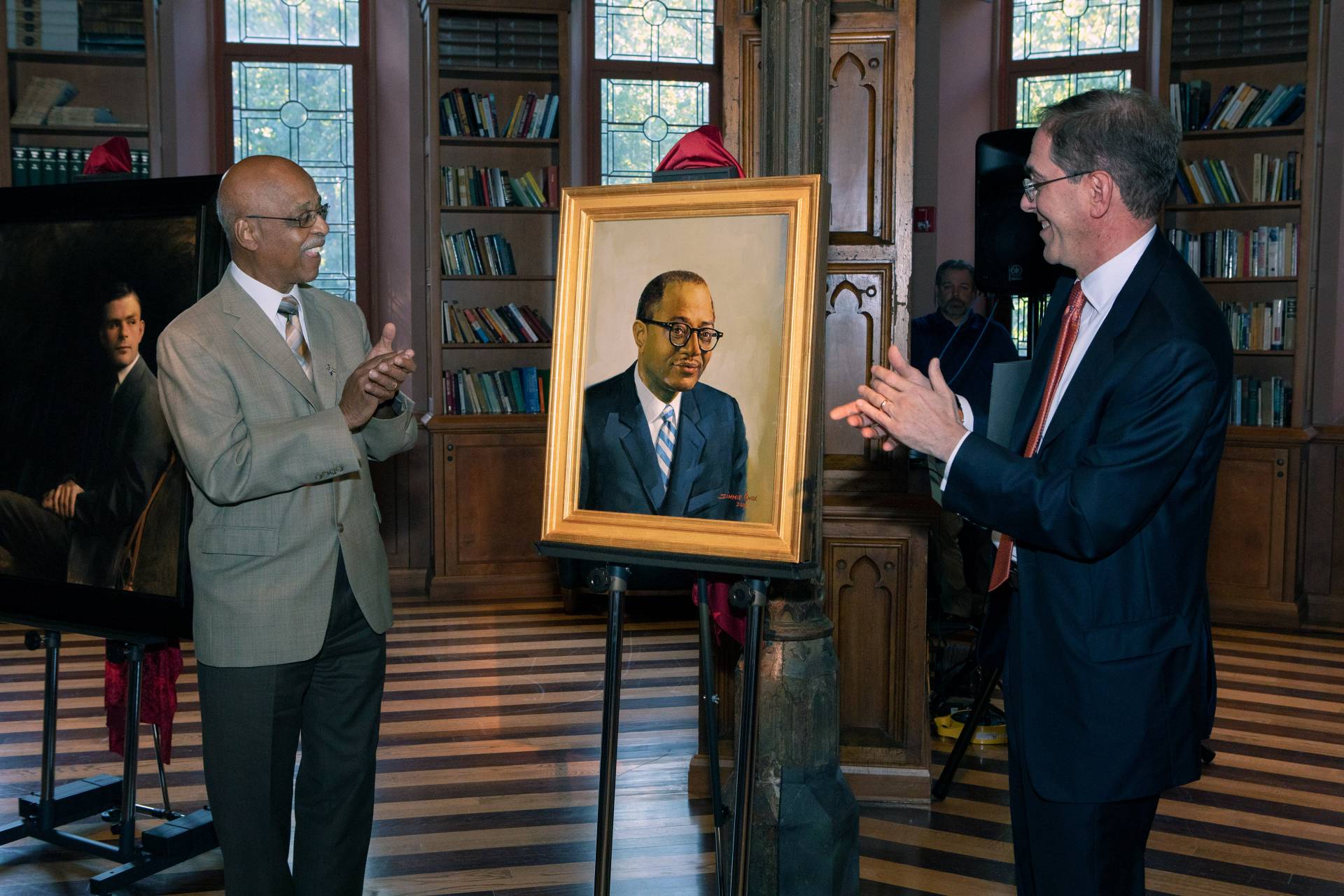 two men clap in front of a painting