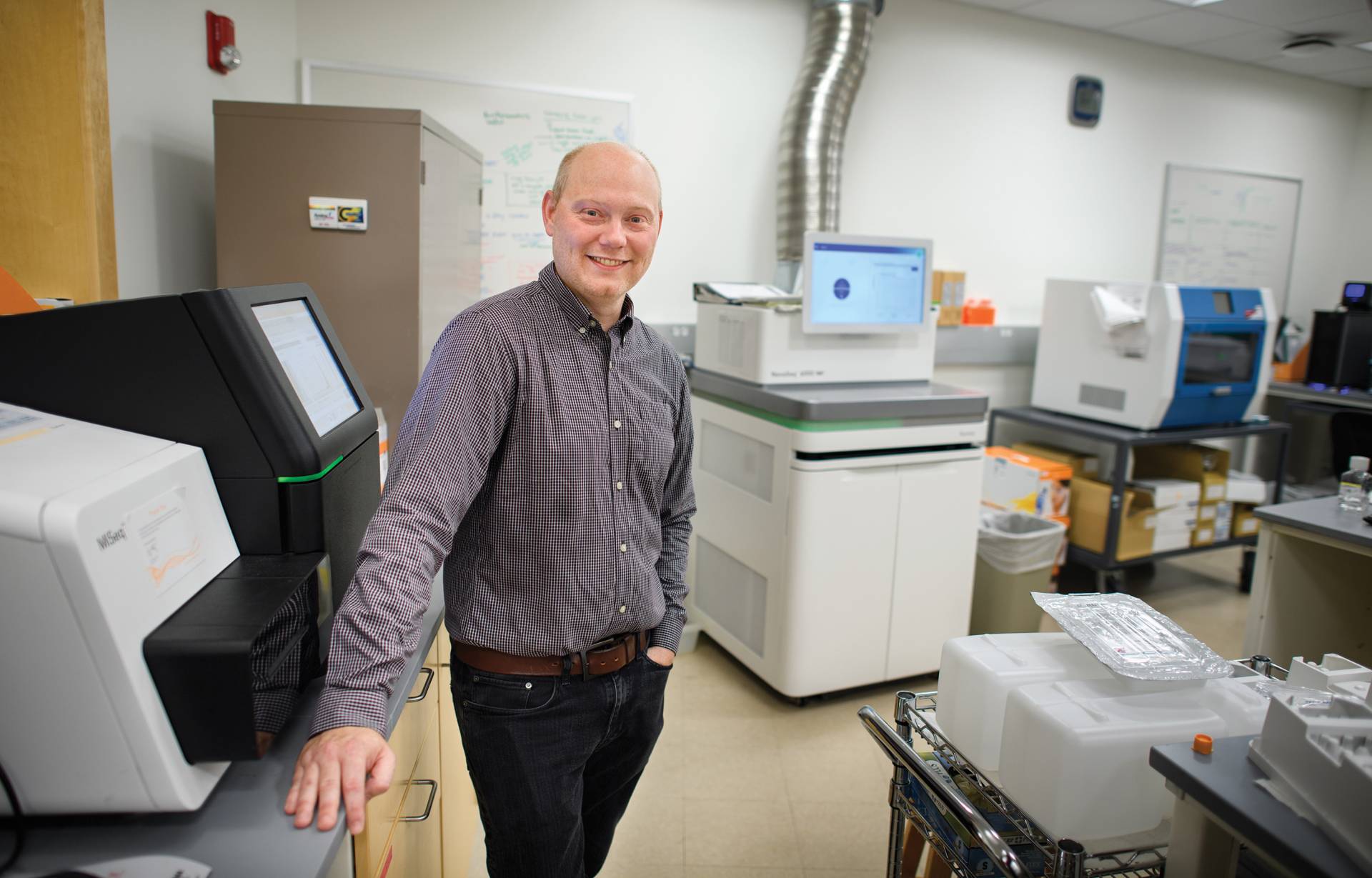 Joshua Akey surrounded by machines that help analyze DNA samples