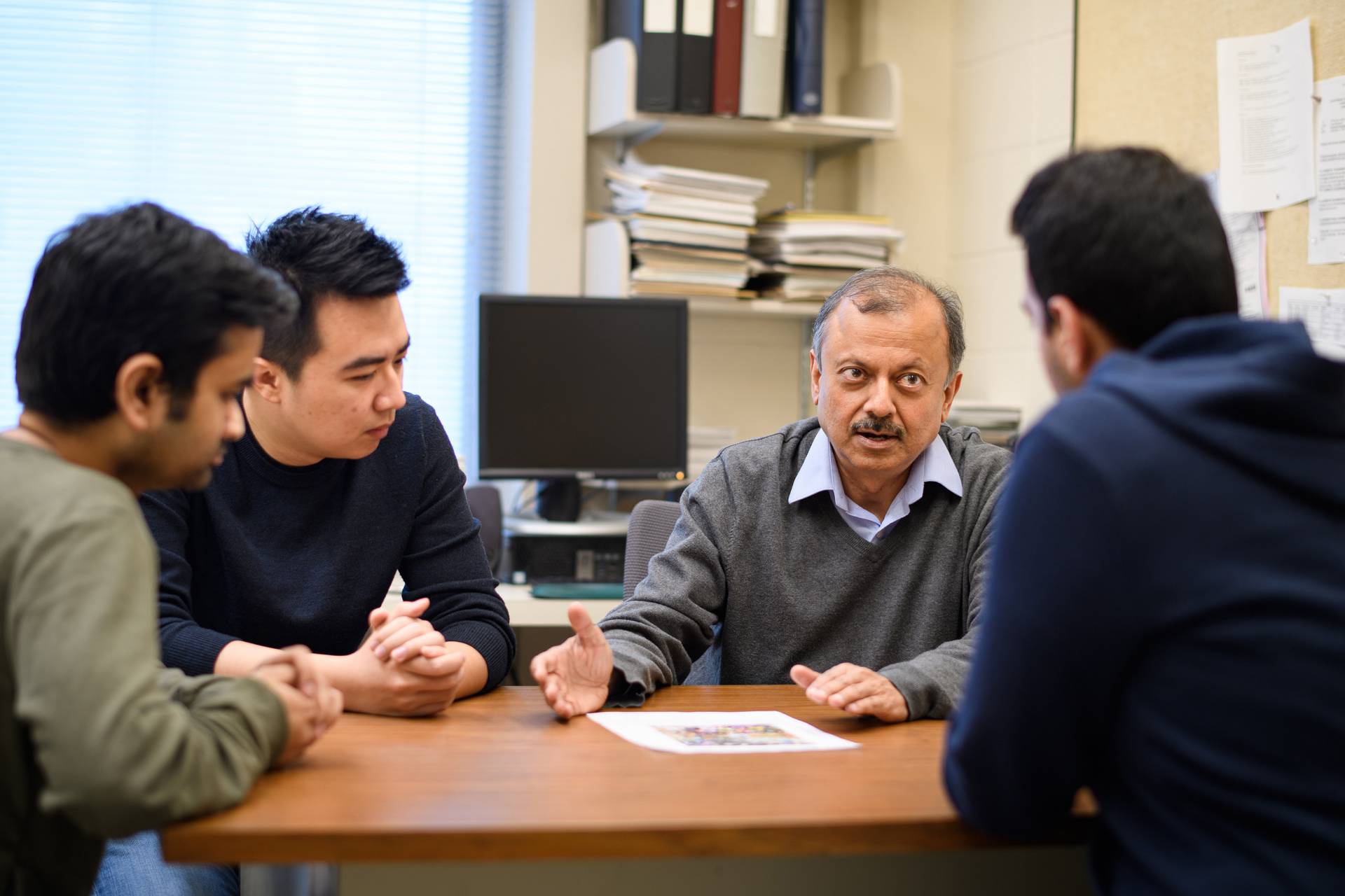 Jha Al speaks over a table to the students in his lab 