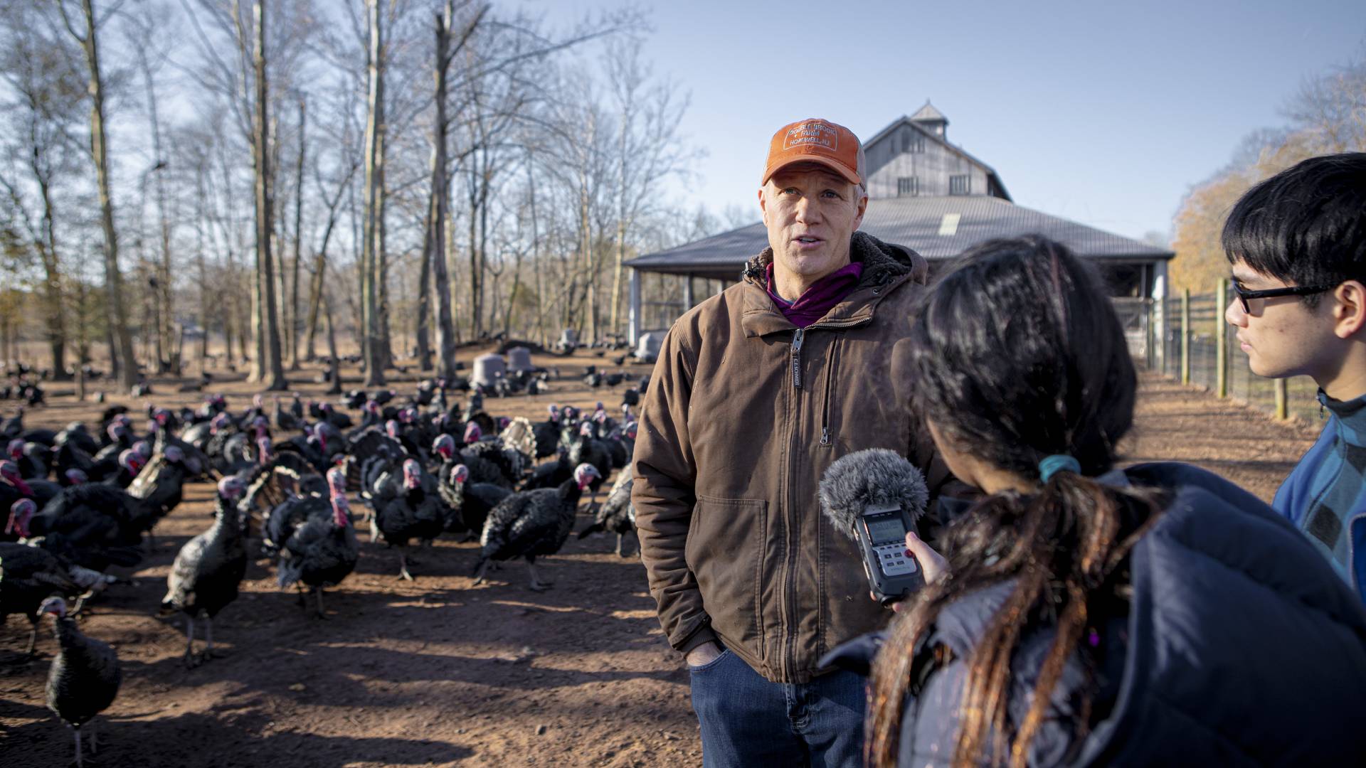 A farmer is interviewed by two students in front of his farm in Hopewell