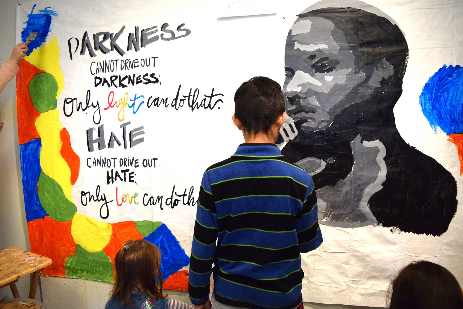 A child helps paint a mural with a quote from Martin Luther King: "Darkness cannot drive out darkness; only the light can do that. Hate cannot drive out hate; only love can do that."