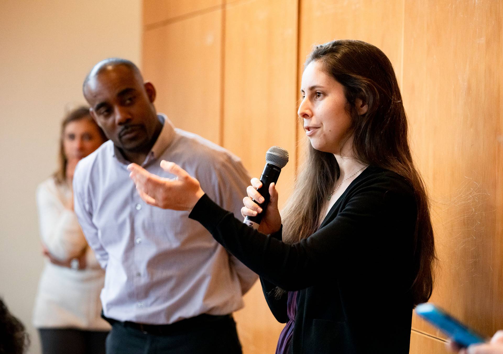 A woman asks a question into a microphone while a man looks on