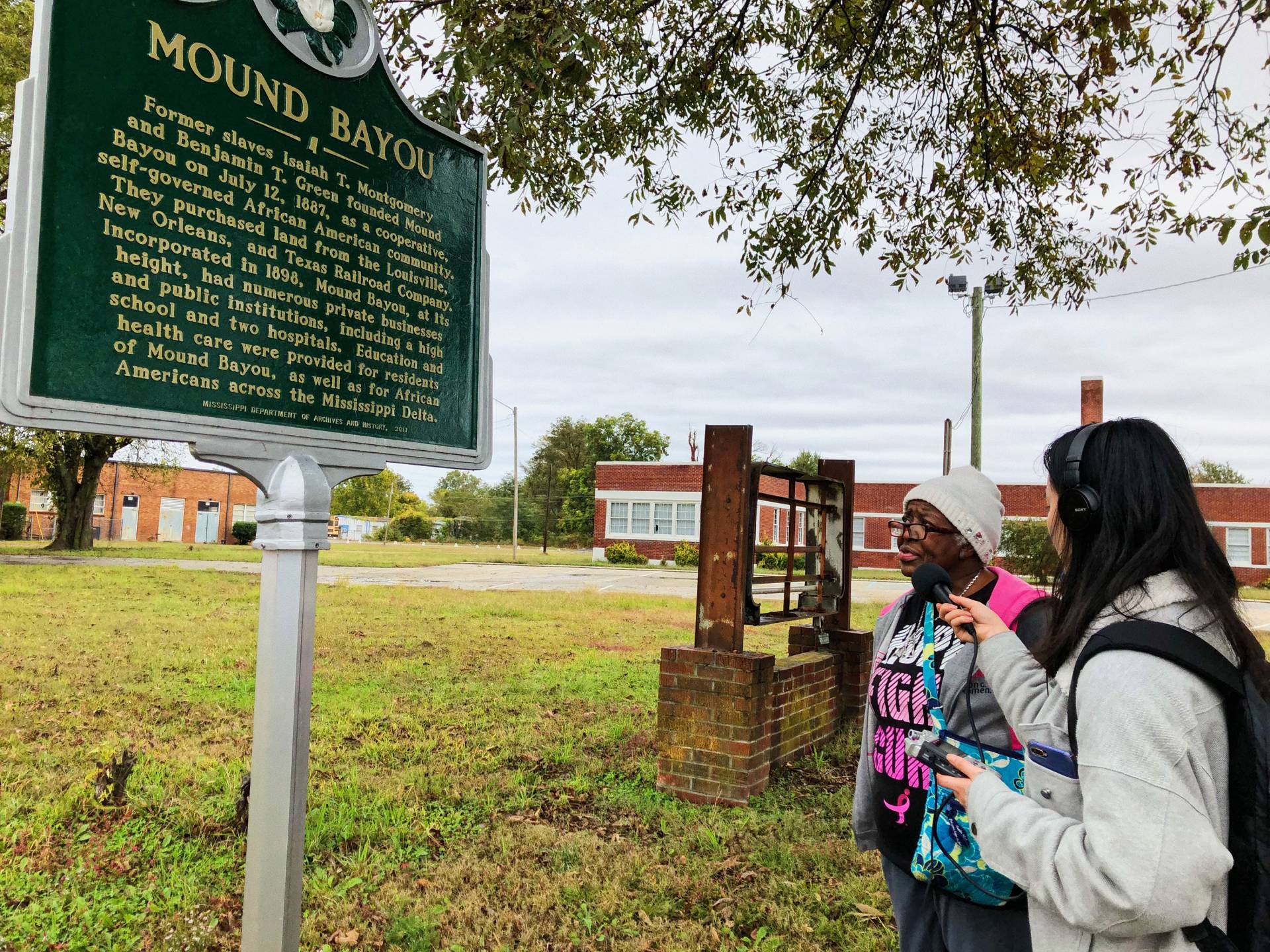 A student interviews the mayor of Mound Bayou next to a historical plaque