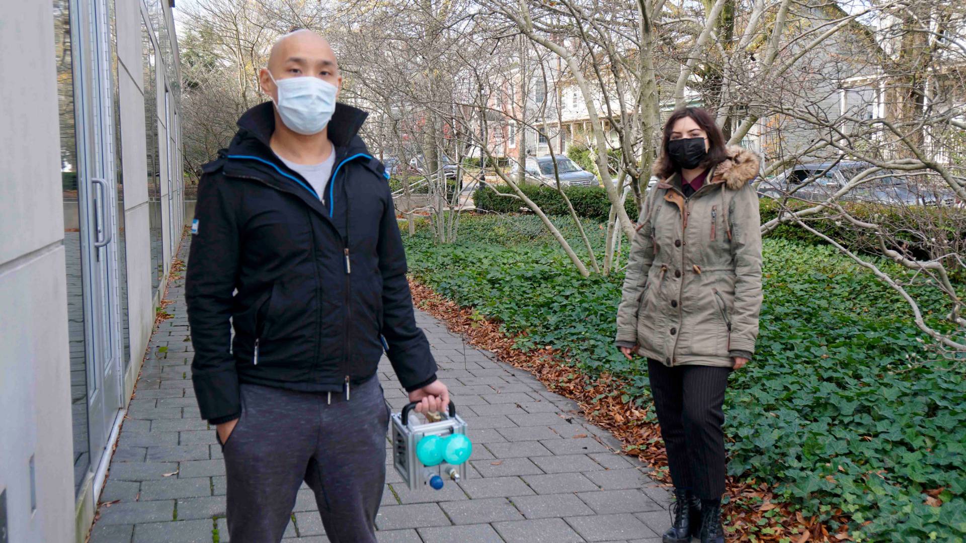 Two graduate students outside the Friend Center, one holding a small ventilator