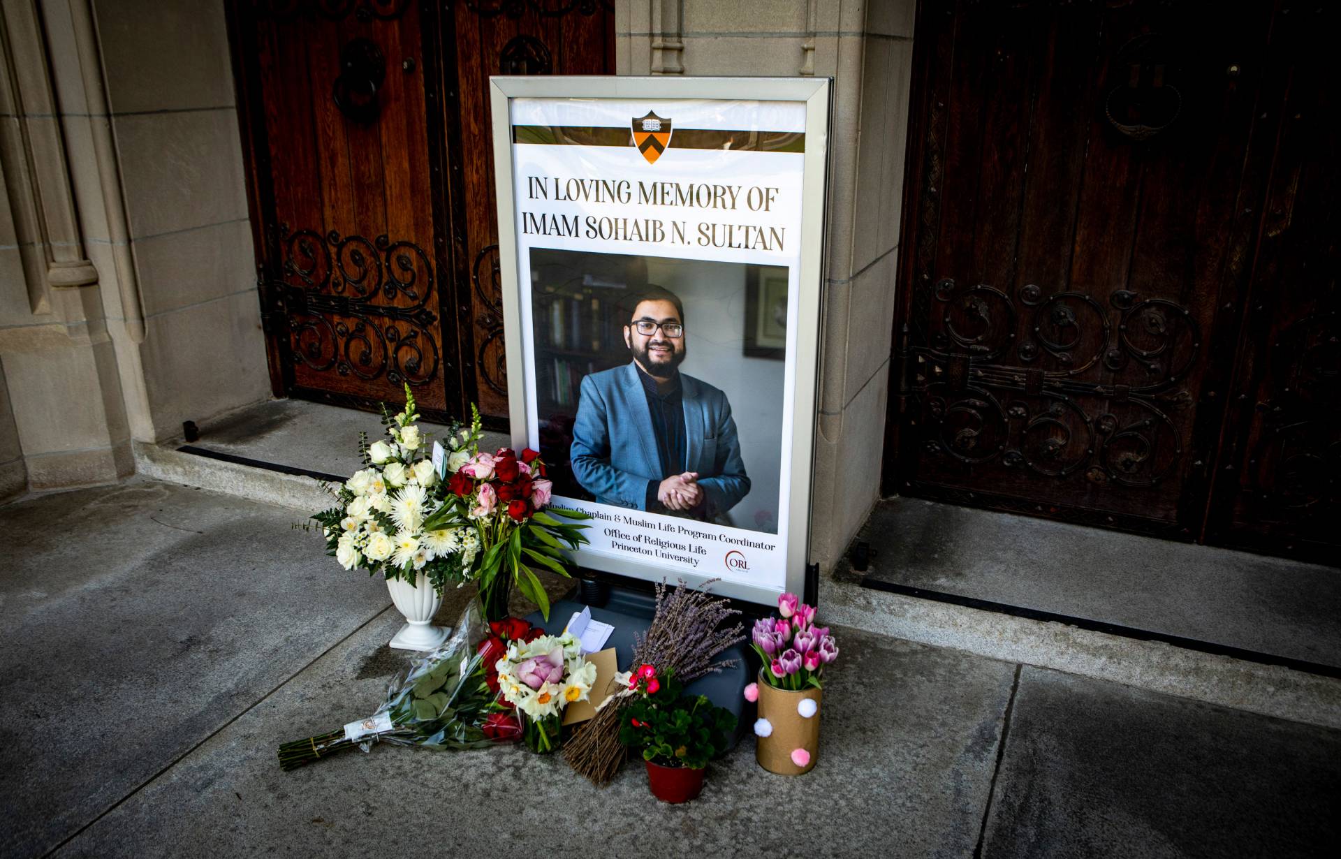 A poster in front of chapel doors, reading, "In Loving Memory of Imam Sohaib N. Sultan" and flowers