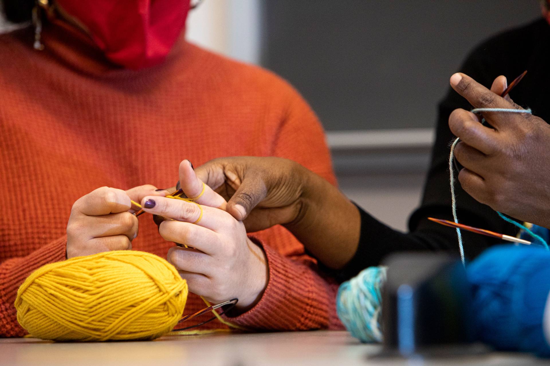 A person knits while another adjusts finger positioning