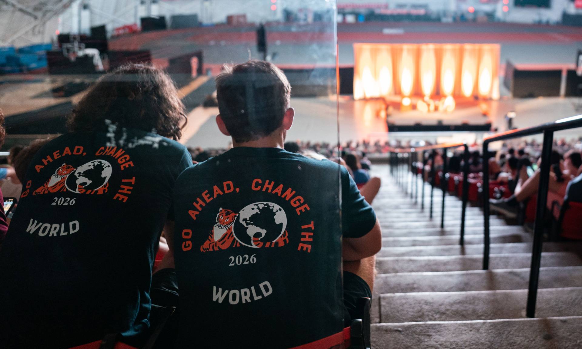 students in the audience wear t-shirts that read "Go ahead. Change the world. 2026"