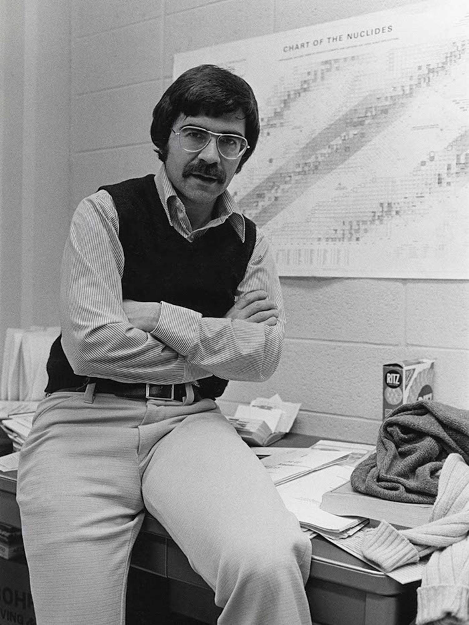 In this black-and-white photo, a young Harold Feiveson sits on top of his desk with his arms crossed.