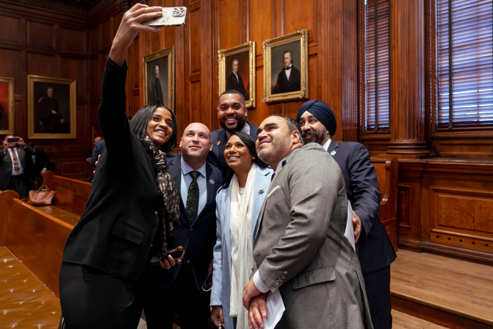 A group pose for a selfie against portraits on the walls of Nassau Hall