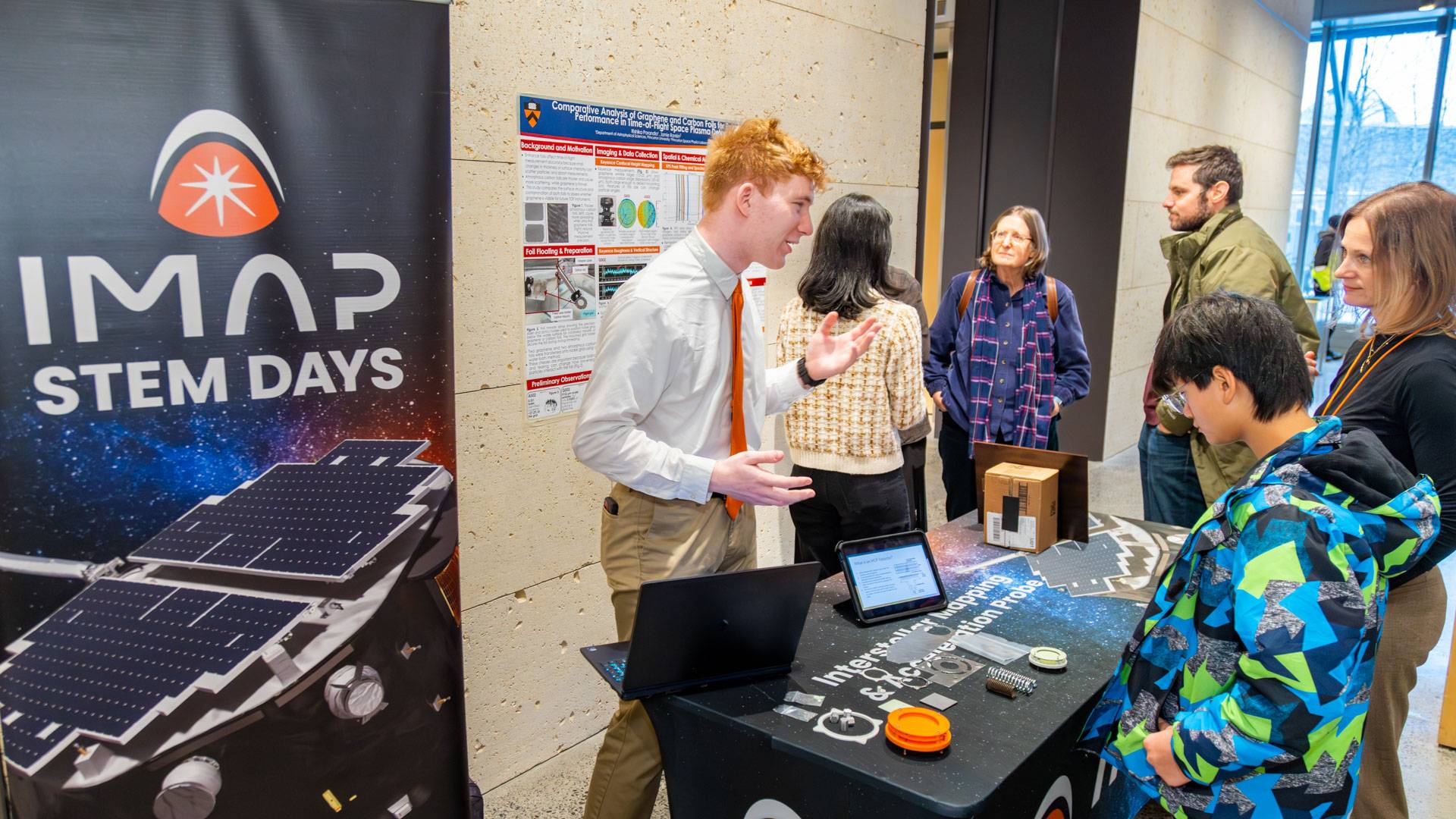 An undergraduate behind a table speaks to gathered listeners.