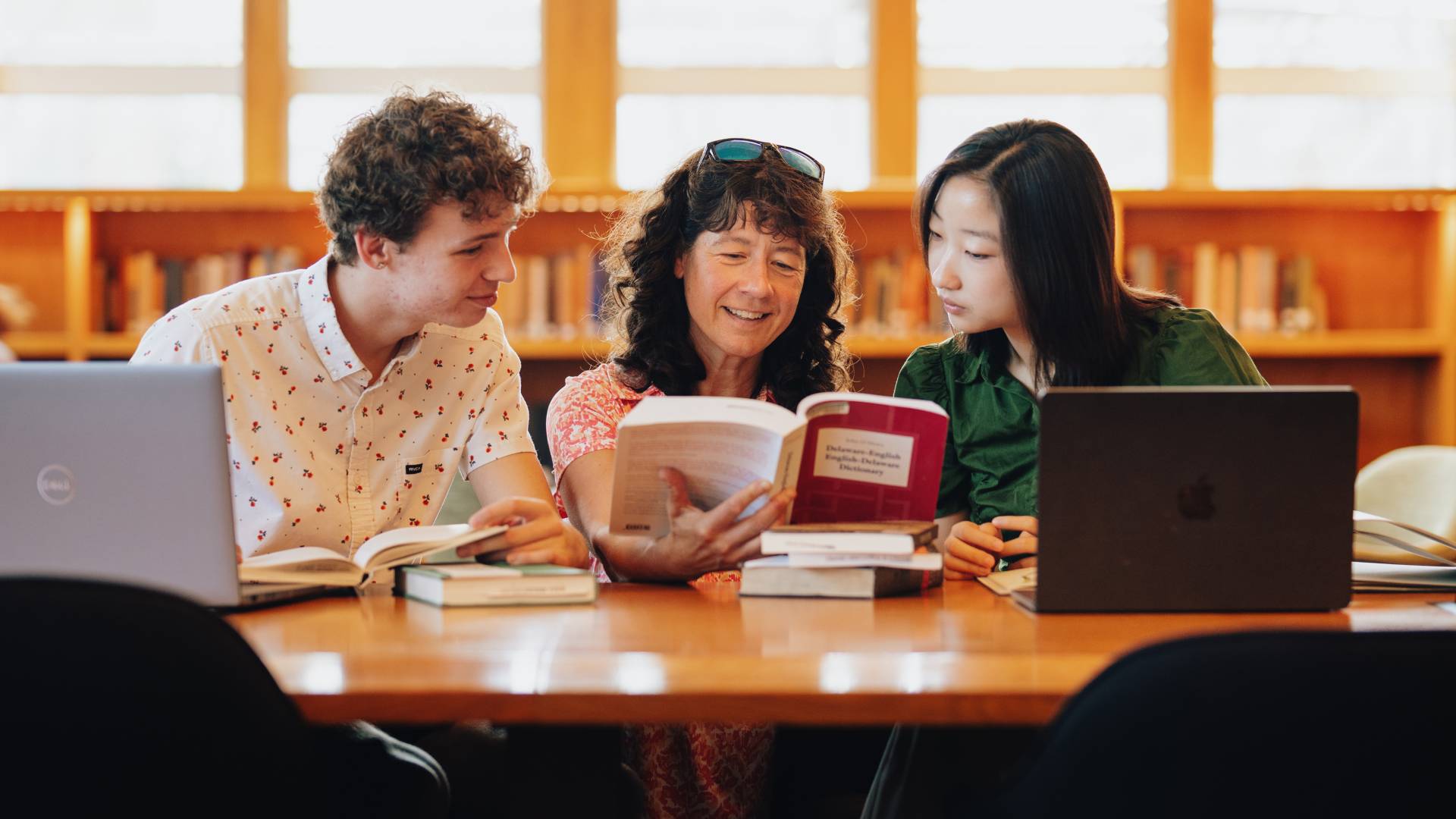Librarian Maria Kochis examines a book with two students.
