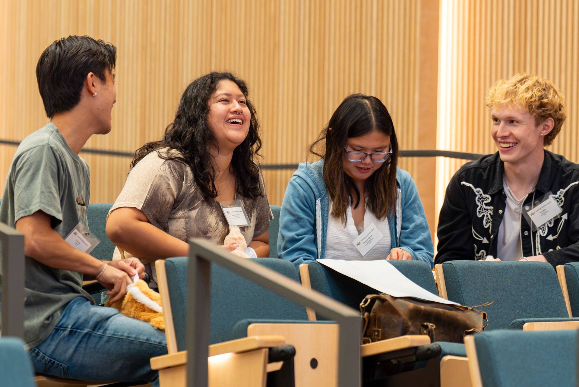 Four graduate students talk together seated in an auditorium.