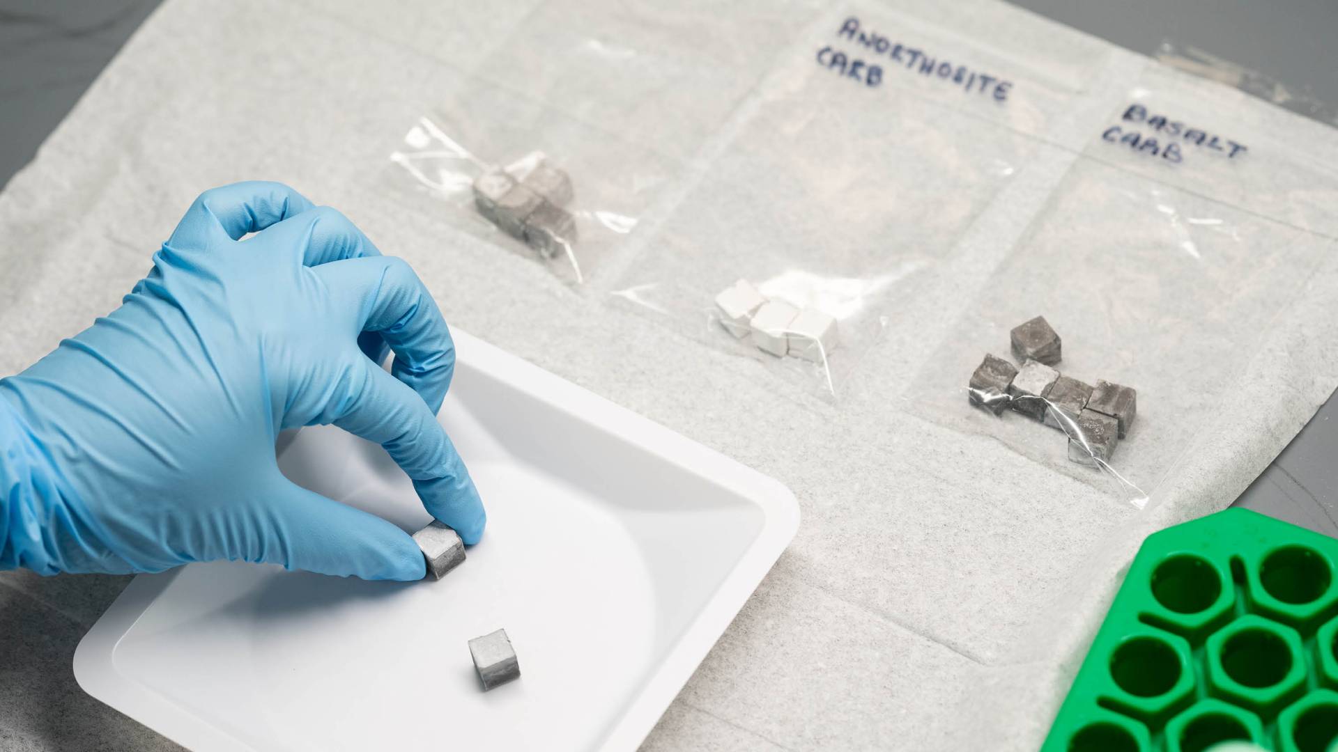A gloved hand prepares cubes of various materials to evaluate their performance as cement-like materials.