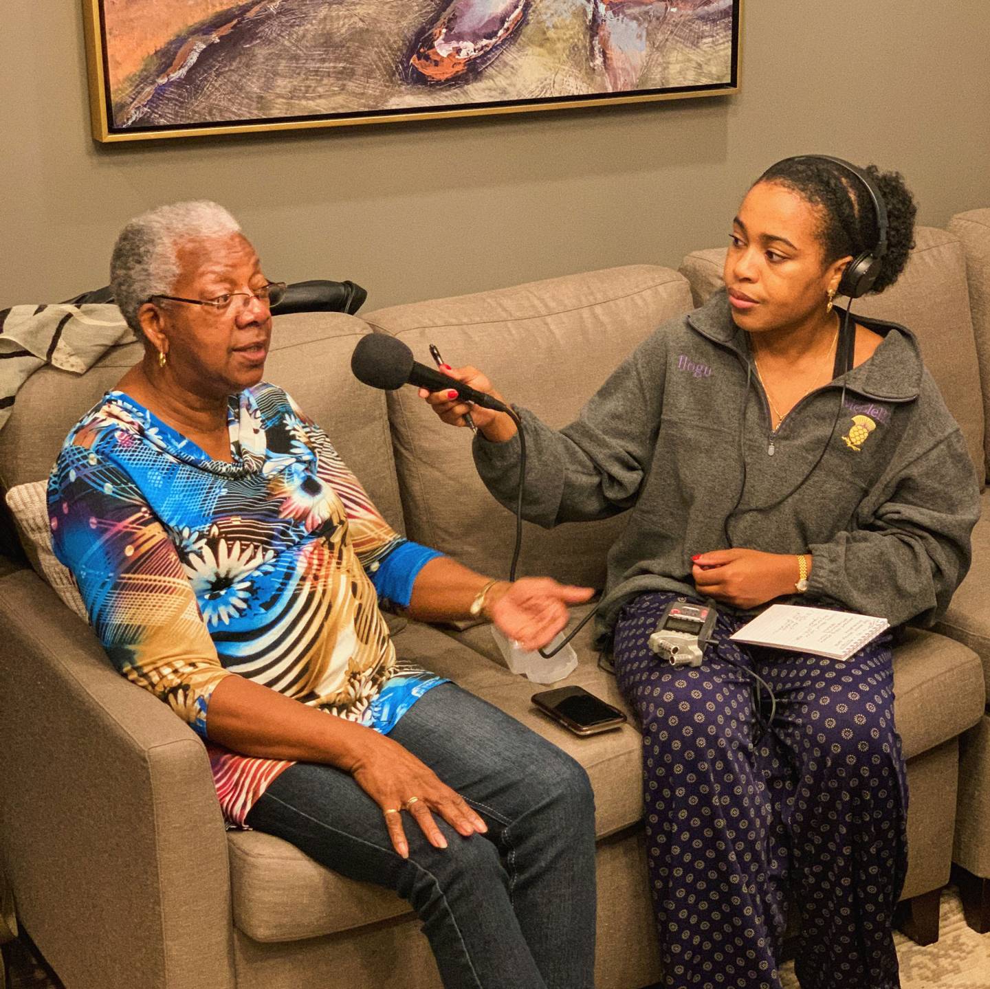 A student interviews a woman on a tan sofa