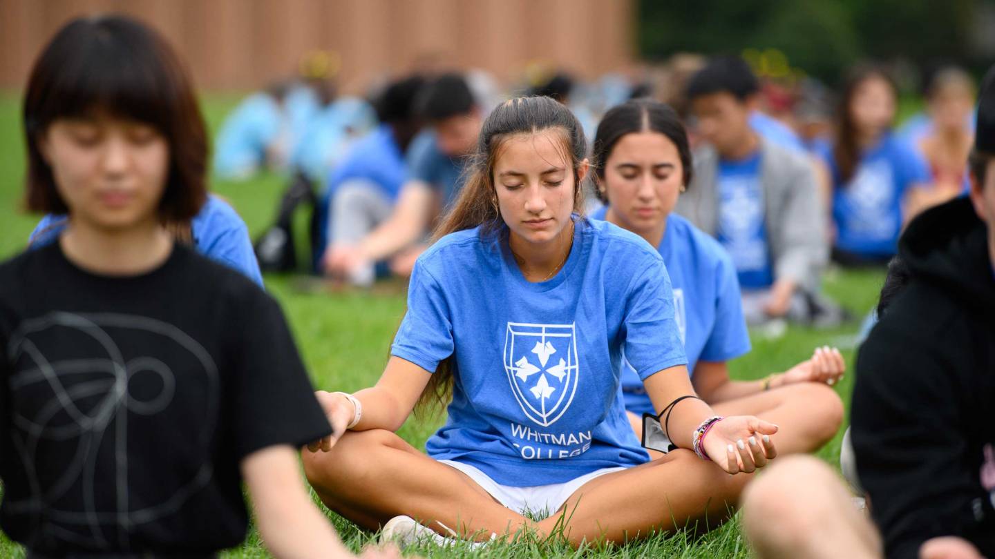 Students from Whitman College sit cross-legged and mediate on the lawn