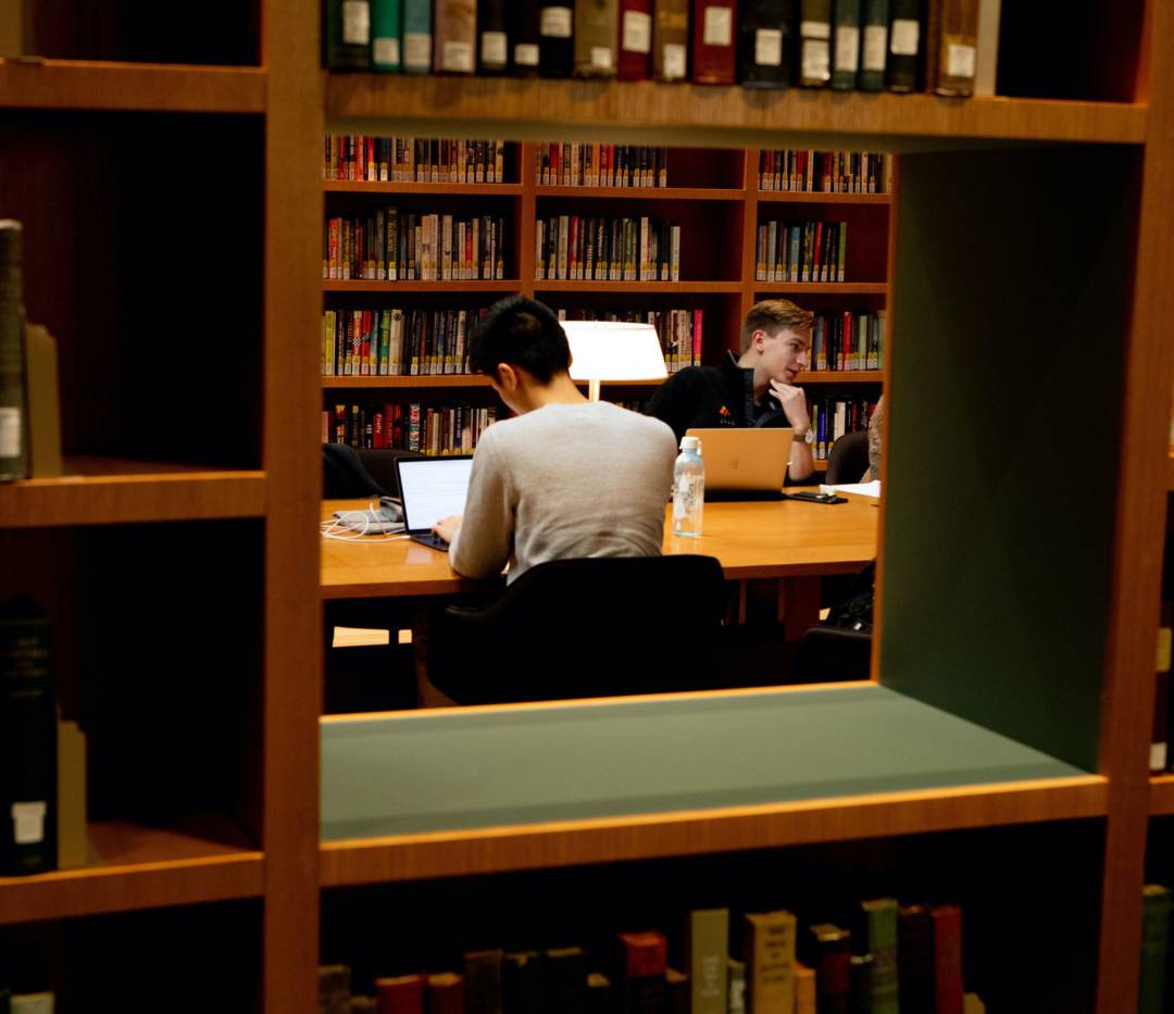 Students studying in library, as seen through opening in book shelves.