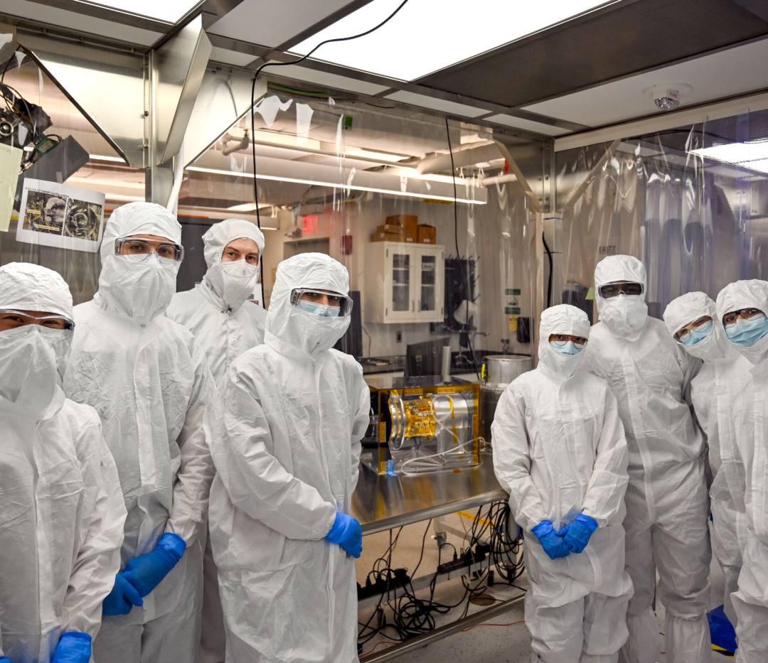 Students wearing white overalls inside a NASA clean room.