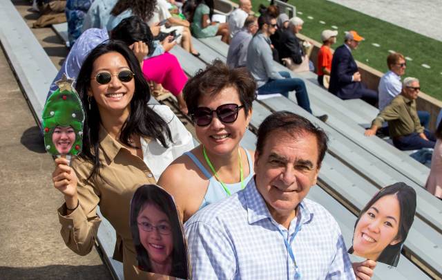 A family sits in the stands with their photo masks of their graduate