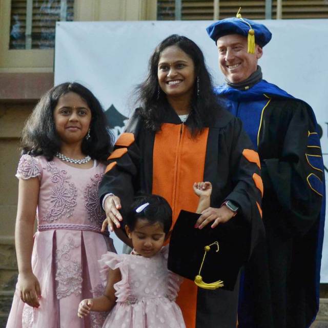 Woman with two daughters poses with adviser at graduate hooding ceremony