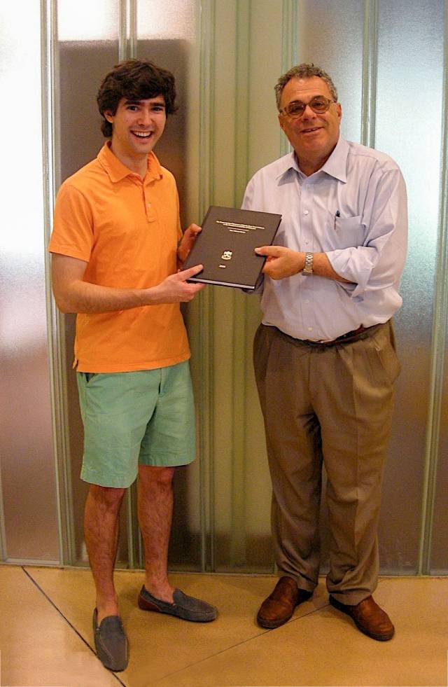A young man in shorts and an older man hold a book between them.